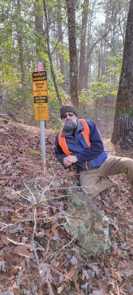 Heath Ledet outdoors beside a national forest property boundary marker